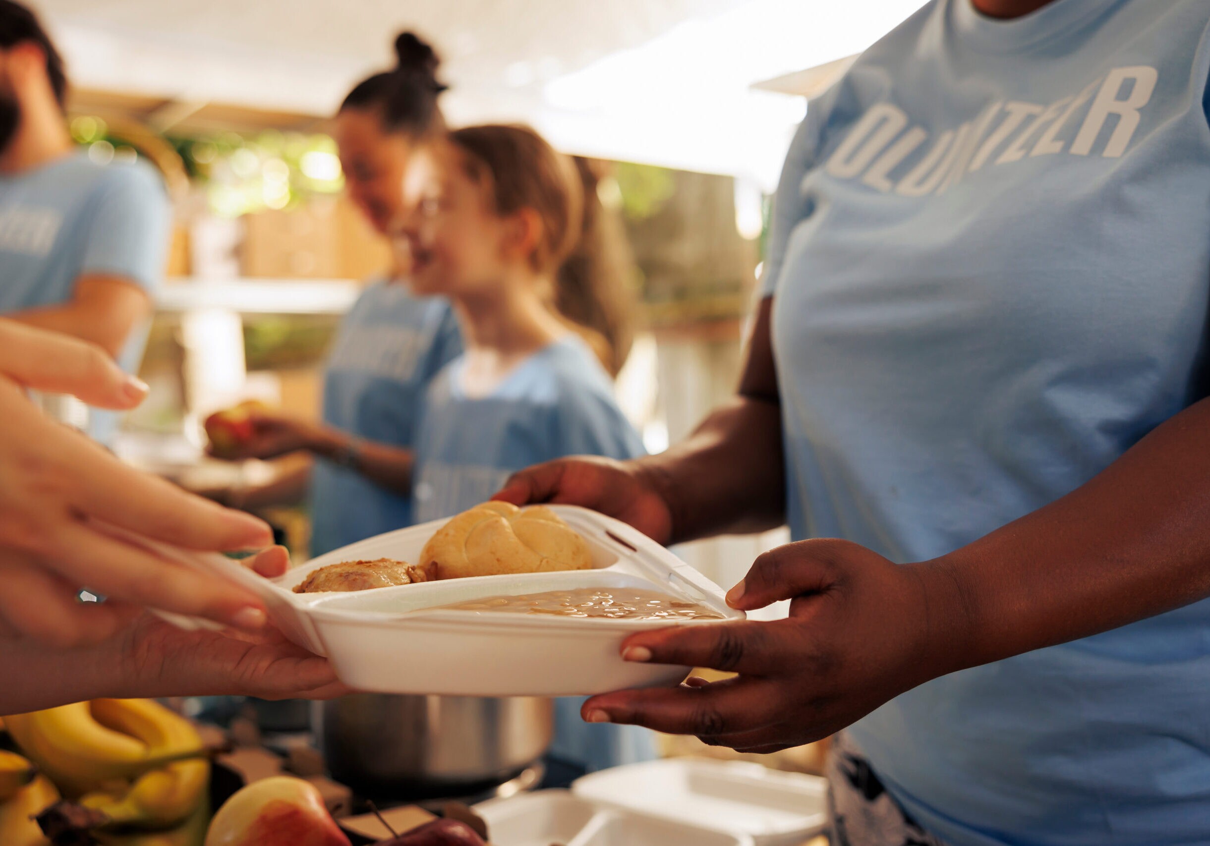 Close-up of a young black woman hands distributing fresh produce to needy homeless people at a food drive. Detailed image of free food being shared to a poor less privileged caucasian person.