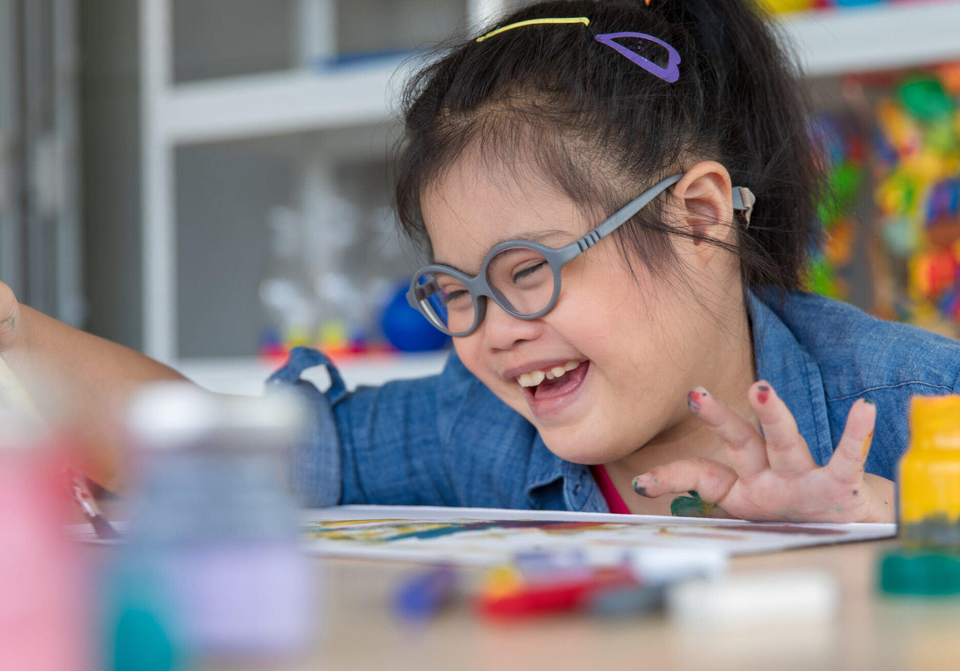 Child finger painting at a table with colorful art supplies in a classroom setting.