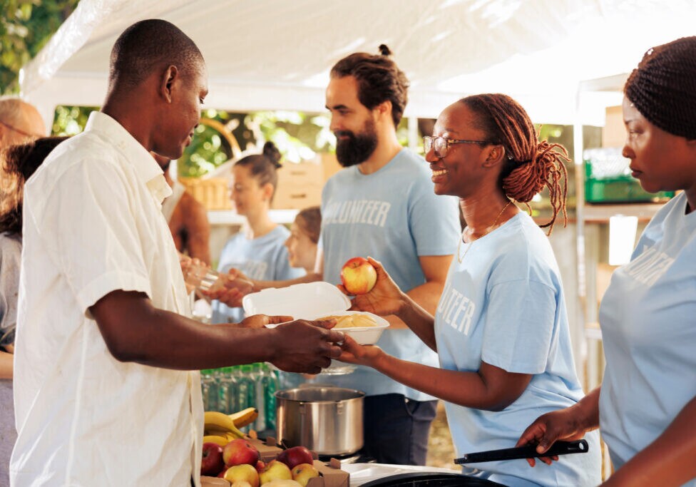 Volunteers serving food and fruit to people at a community event.
